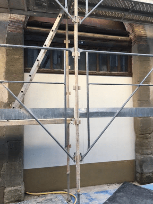 Échafaudage devant un mur blanc et une fenêtre ancienne numéro 3 lors de travaux de rénovation de façade.