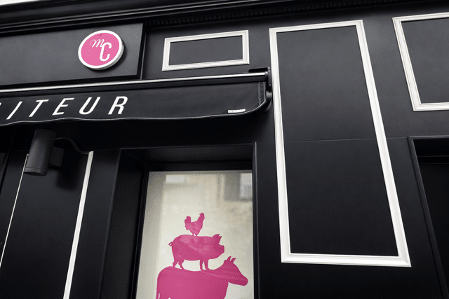 Façade noire moderne de boucherie avec logo MC rose et silhouettes d'animaux empilées en vitrine Traiteur.