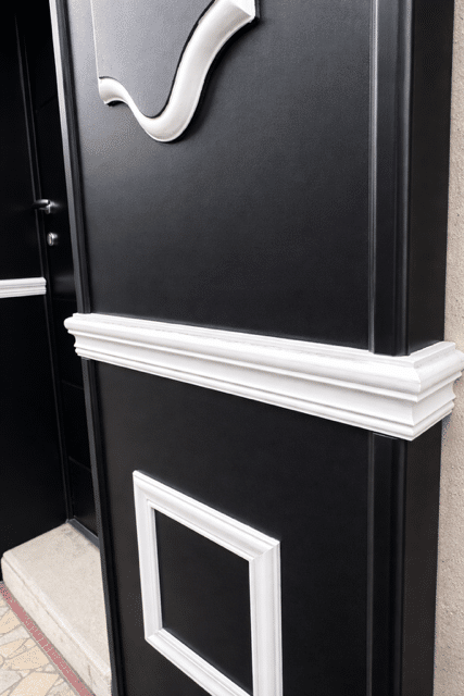Mur noir mat avec moulures décoratives blanches style boiserie, détail élégant pour une façade moderne.
