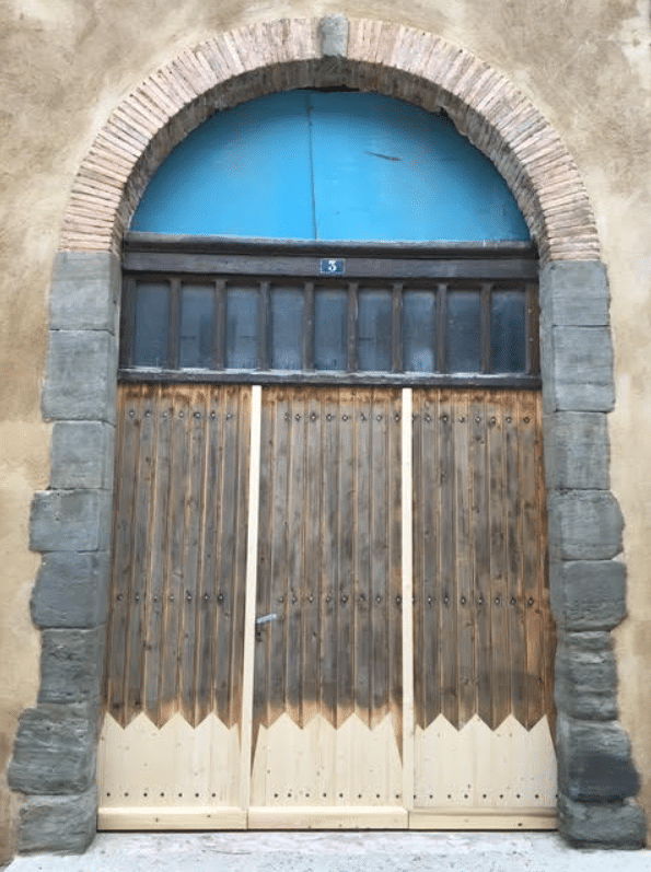 Porte rustique sous arche de brique et pierre, imposte bleue avec numéro 3 et soubassement en bois clair restauré.