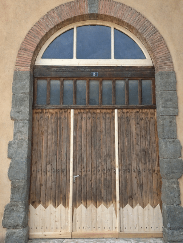 Porte ancienne en bois sous arche de briques, numéro 3, imposte vitrée et bas de porte rénové en zigzag.