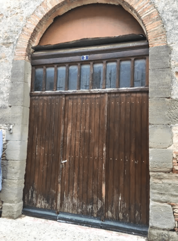 Grande porte ancienne en bois brun sous une arche de pierre avec le numéro 3 et des fenêtres à imposte.