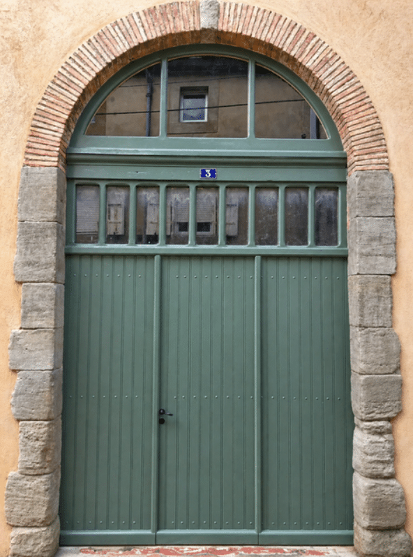 Porte en bois vert sauge numéro 3 sous une arche en brique et pierre. Fenêtres à imposte vitrée.