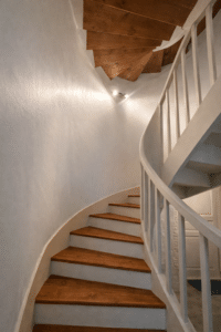 Escalier en colimaçon avec marches bois, murs blancs arrondis et garde-corps épuré.