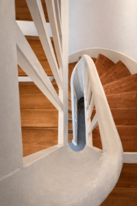 Vue plongeante d'un escalier en colimaçon avec marches en bois et garde-corps blanc incurvé.