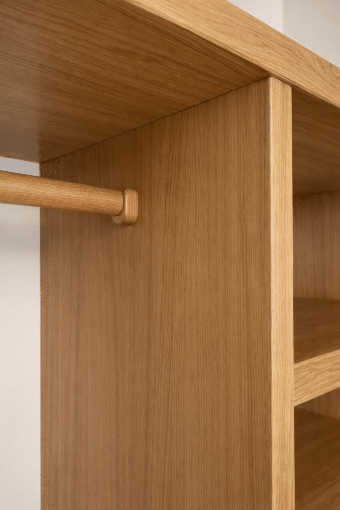 Détail d'une penderie en chêne clair avec tringle en bois et étagères intégrées.