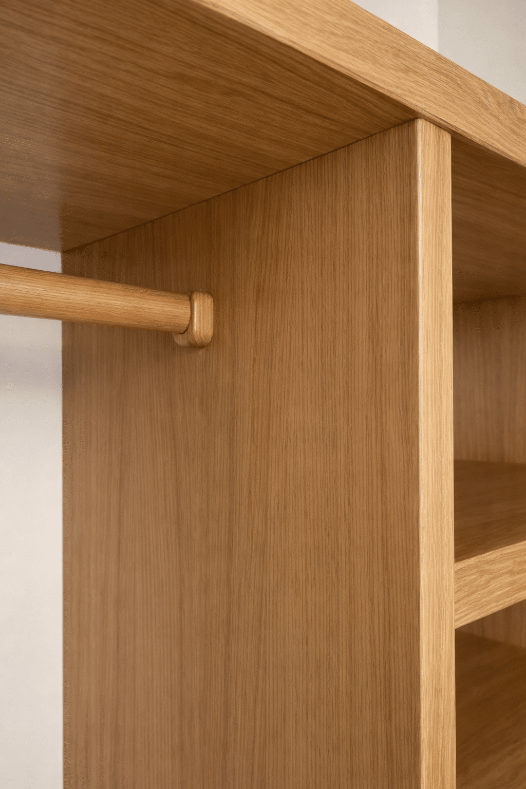 Détail d'une penderie en chêne clair avec tringle en bois et étagères intégrées.