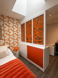 Chambre design orange et blanc avec cloison vitrée motif corail et papier peint floral.