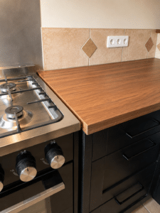 Cuisinière inox, plan de travail effet bois et meubles noirs. Crédence carrelée avec prises murales.