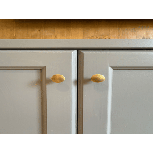Portes de placard grises et boutons ovales en laiton sous plan de travail en bois.