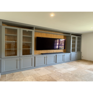 Meuble TV mural gris, vitrines latérales, fond bois et carrelage beige.